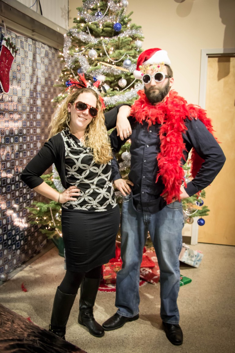Cory posing in front of a Christmas tree with a woman wearing Christmas props